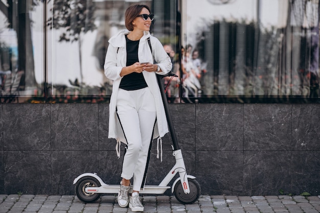 Young woman riding scotter in town and using phone