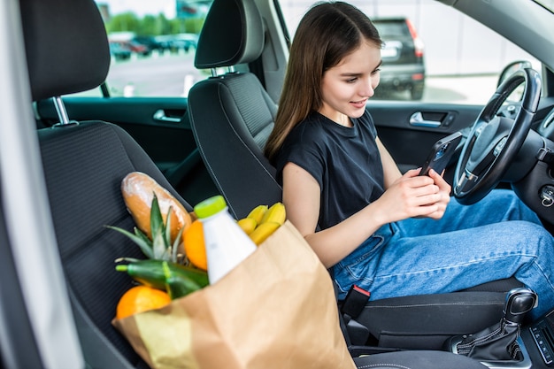 屋外駐車場で食べ物でいっぱいのショッピングカートに乗って若い女性