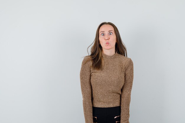 Young woman rolling eyes in gold gilded sweater and black pants and looking amused