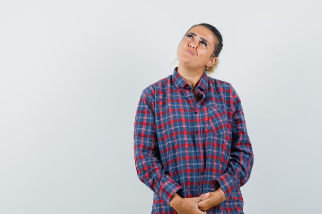 Young woman rubbing hands and thinking about something in checked shirt and looking pensive. front view.