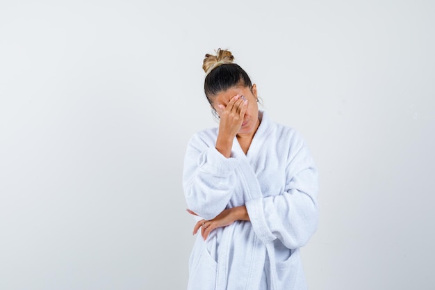 Young woman rubbing her forehead in bathrobe and looking exhausted