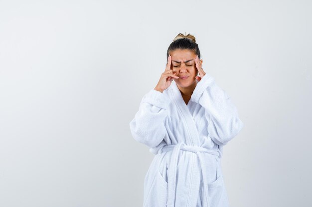 Young woman rubbing her temples in bathrobe and looking fatigued