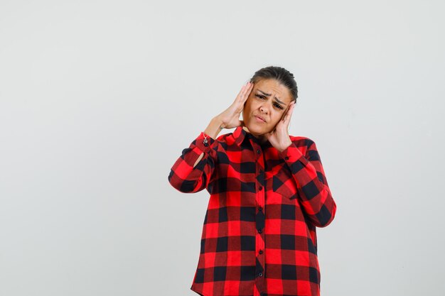 Young woman rubbing her temples in checked shirt and looking tired , front view.