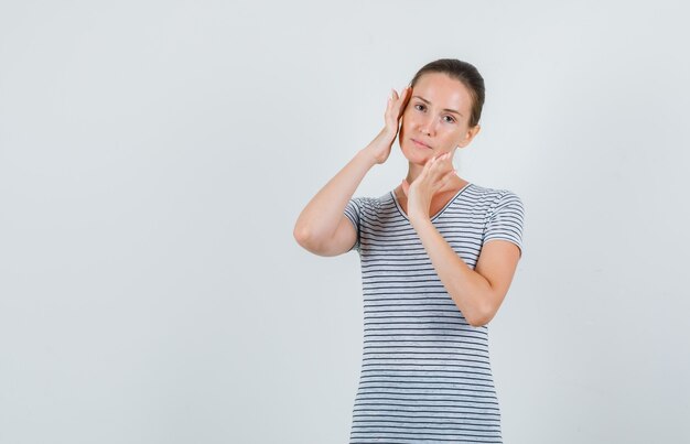 Tシャツでこめかみをこすり、リラックスして見える若い女性、正面図。