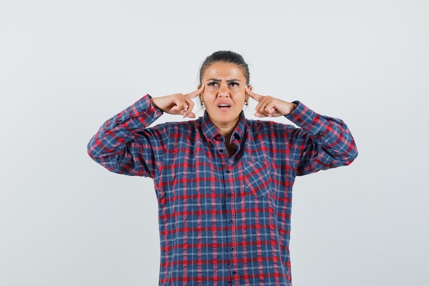 Foto gratuita giovane donna sfregamento tempie e pensando a qualcosa in camicia a quadri e guardando pensieroso. vista frontale.