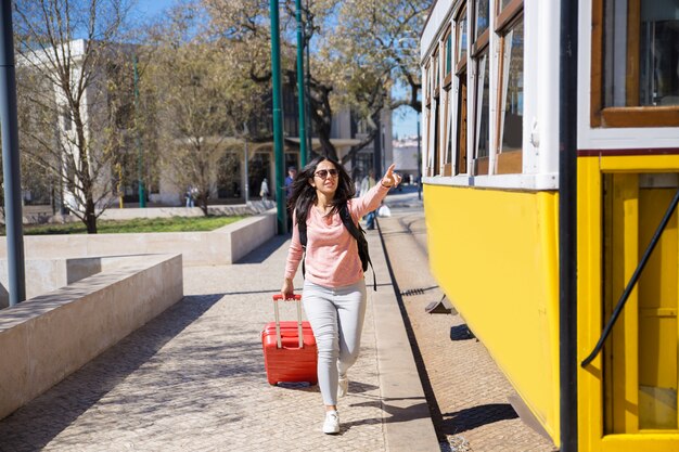 Young woman running after trolleybus and pulling trolley case