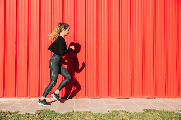 Young woman running near red wall