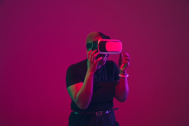 Young woman's portrait with VR glasses on purple pink wall in neon lights