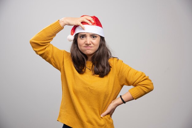 Молодая женщина в красной шляпе Санта-Клауса позирует над белой стеной.