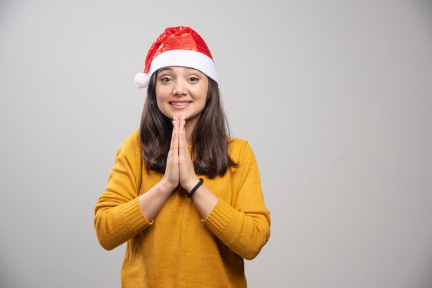 Young woman in Santa hat feeling grateful on gray wall. 