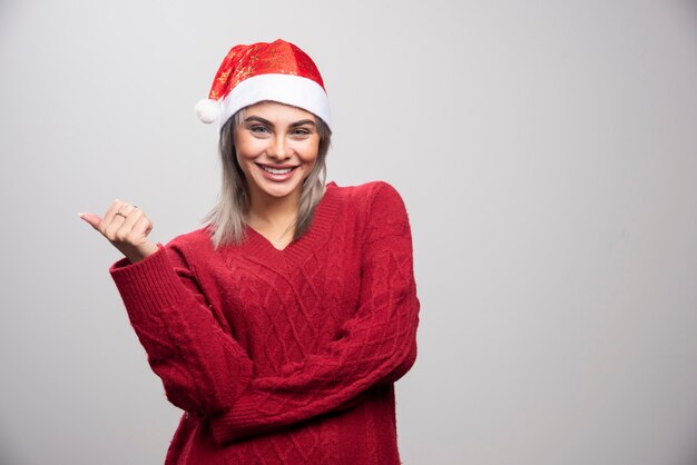 회색 배경에 포즈를 취하는 산타 모자에 젊은 여자.