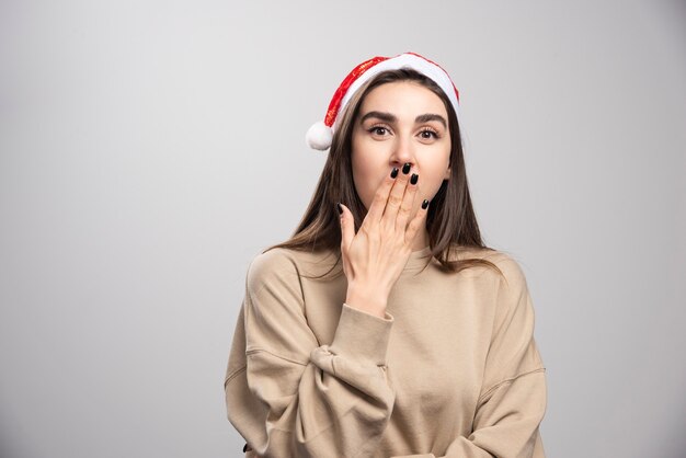 Young woman in Santa's hat covering her mouth and posing.