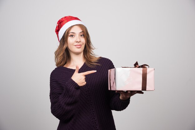 Young woman in Santa's hat pointing at a present .