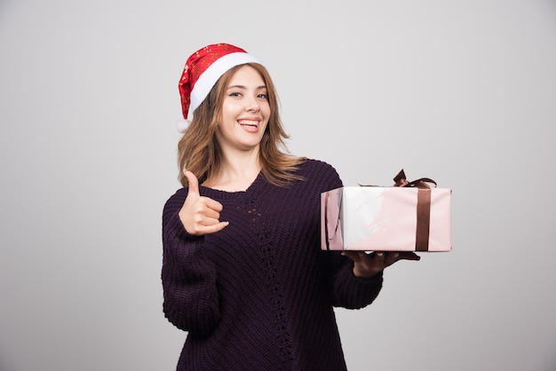 Young woman in Santa's hat with a present showing a thumb up .