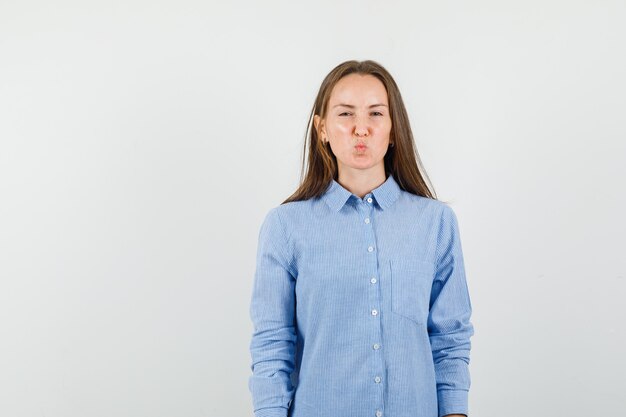 Молодая женщина хмурится, скручивая губы, в синей рубашке и выглядит обиженной.