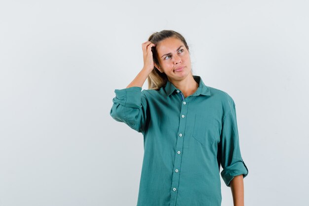 Young woman scratching head while thinking about something in green blouse and looking pensive