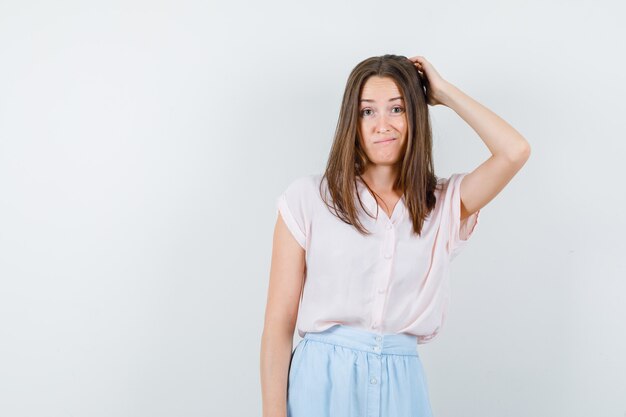 Young woman scratching head while thinking in t-shirt, skirt and looking hesitant , front view.