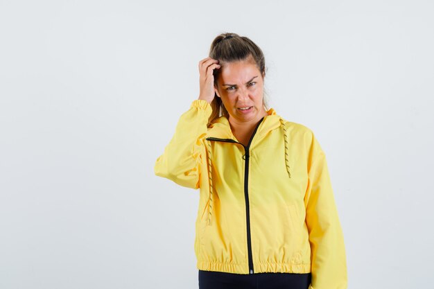 Young woman scratching her head in yellow raincoat and looking troubled