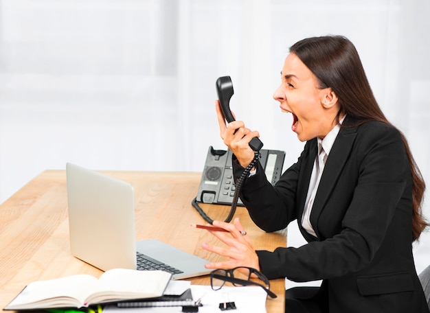 Free photo young woman screaming on telephone at workplace