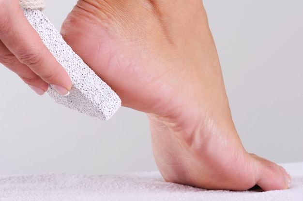 Young woman scrubbing her foot by pumice in a beauty salon