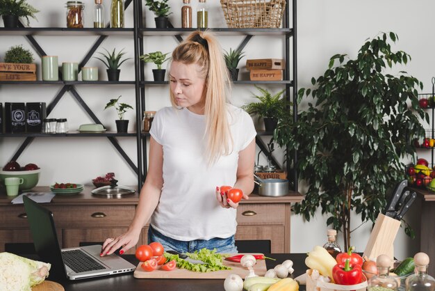 Молодая женщина, поиск рецепт на ноутбуке на кухне