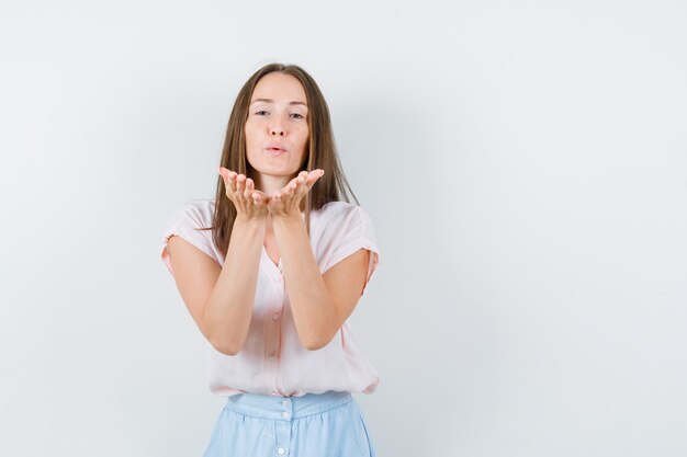 Young woman sending air kiss in t-shirt, skirt front view.