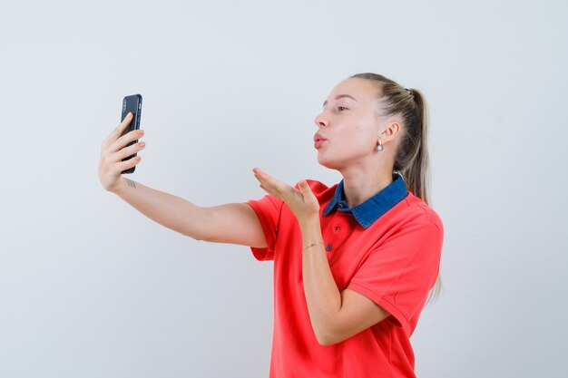 Молодая женщина посылает воздушный поцелуй, принимая селфи в футболке