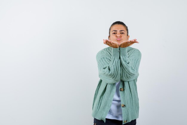 Young woman sending kisses in white t-shirt and mint green cardigan and looking attractive