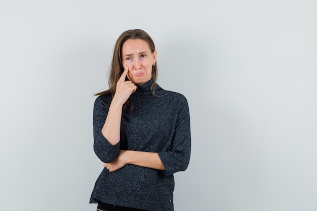 Young woman in shirt holding finger on cheek and looking sad 