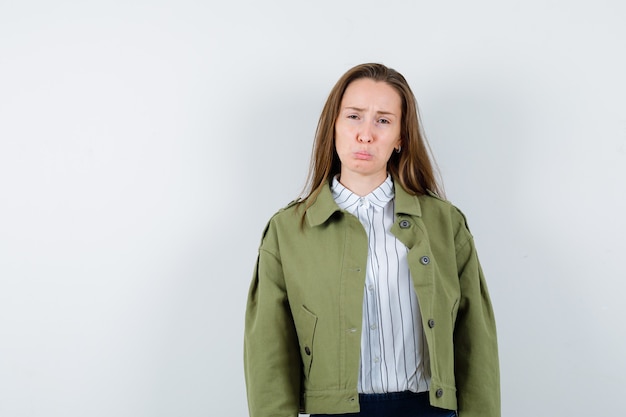 Young woman in shirt, jacket curving lips, frowning face and looking downcast, front view.
