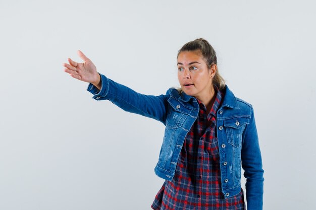 Young woman in shirt, jacket giving instructions by stretching arm , front view.