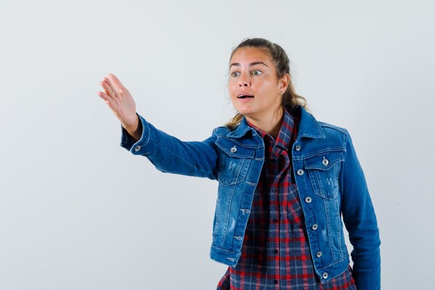 Young woman in shirt, jacket giving instructions by stretching hand , front view.