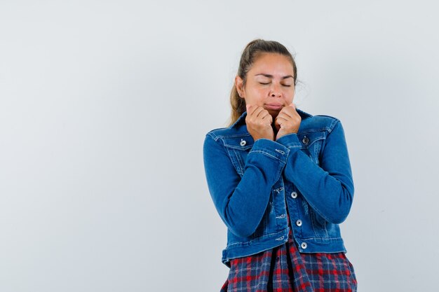 Young woman in shirt, jacket posing while pulling her collar and looking peaceful , front view.