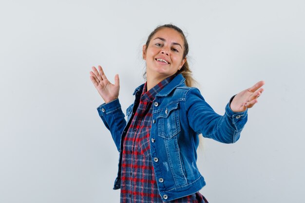 Young woman in shirt, jacket posing while spreading arms and looking jolly , front view.