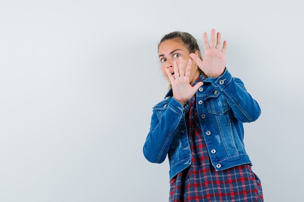 Free photo young woman in shirt, jacket showing stop gesture and looking scared , front view.