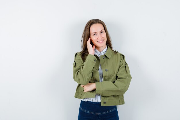 Young woman in shirt, jacket touching her skin on cheek and looking delicate , front view.