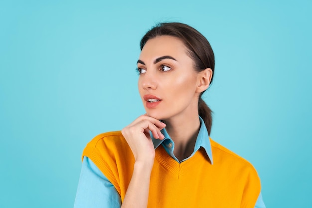 Young woman in a shirt and an orange vest on a turquoise background looks thoughtfully to the side