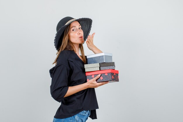 셔츠, 반바지, 모자 공기 키스를 보내는 동안 선물 상자를 들고있는 젊은 여자.