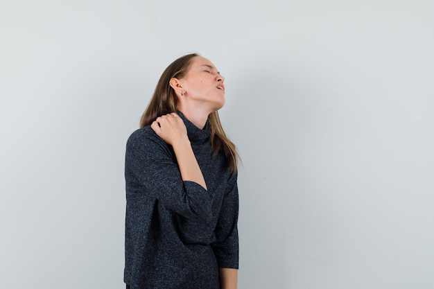Young woman in shirt suffering from neck pain and looking fatigued 