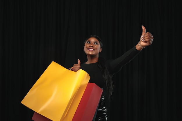 Free photo young woman shopping with colorful packs on black wall