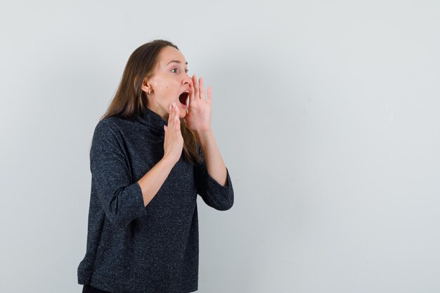 シャツを着て口の近くで手で叫んで興奮している若い女性