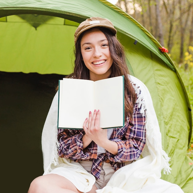 Young woman showing book near tent