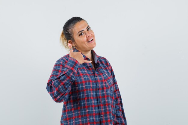 Young woman showing call me gesture in checked shirt and looking pretty. front view.