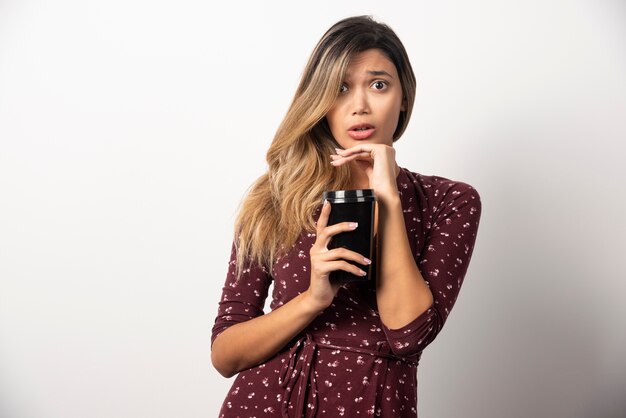 Young woman showing a cup of drink on white wall. 