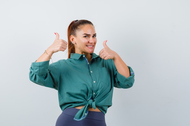 Young woman showing double thumbs up in green shirt and looking glad , front view.