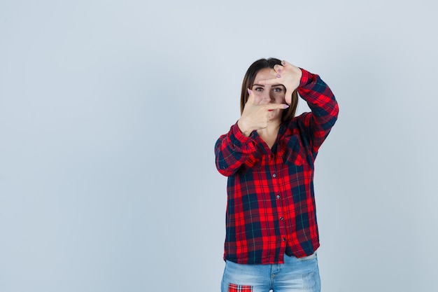 Young woman showing frame gesture in checked shirt and looking confident. front view.