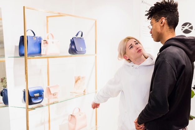 Free photo young woman showing a handbag on shelf she wants to buy from boyfriend