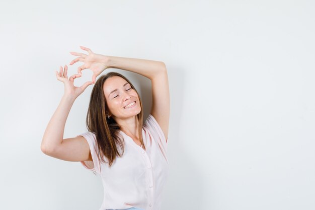 Young woman showing heart gesture and smiling in t-shirt, front view.