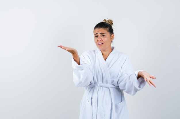 Young woman showing helpless gesture in bathrobe and looking hopeless
