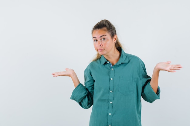 Young woman showing helpless gesture in blue shirt and looking confused